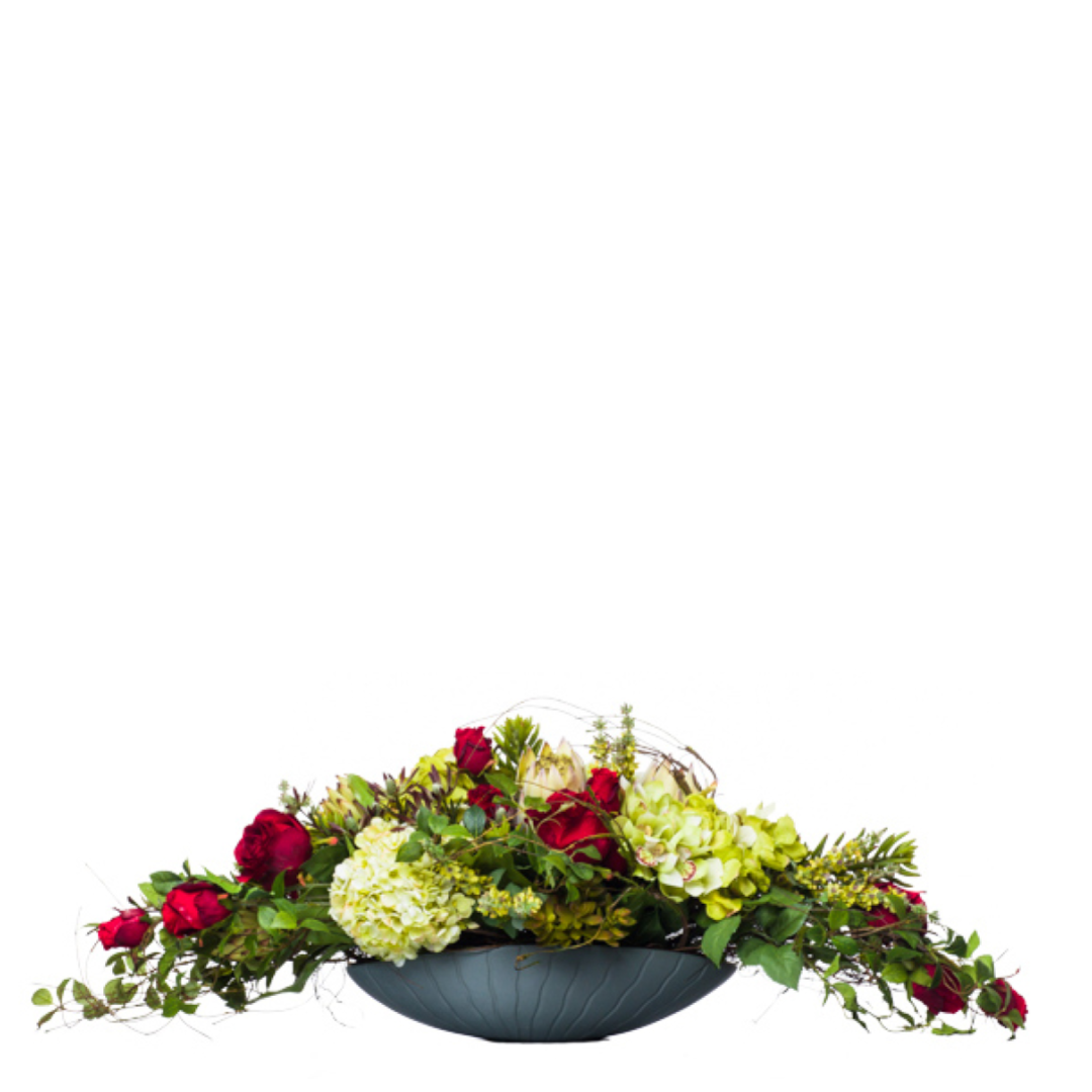 Artificial floral arrangement with red roses, protea, and greenery in a black bowl