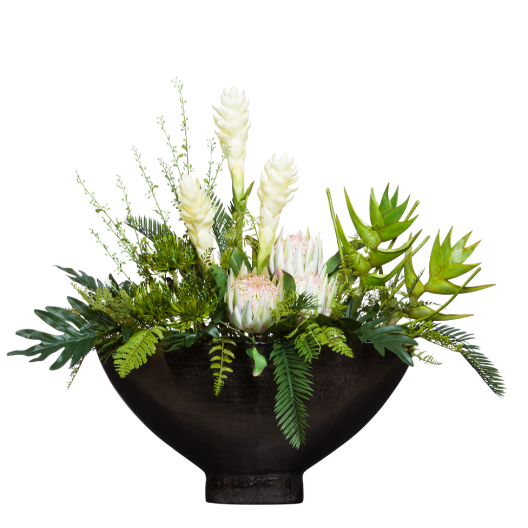 Artificial tropical flower arrangement in a black bowl with proteas and greenery