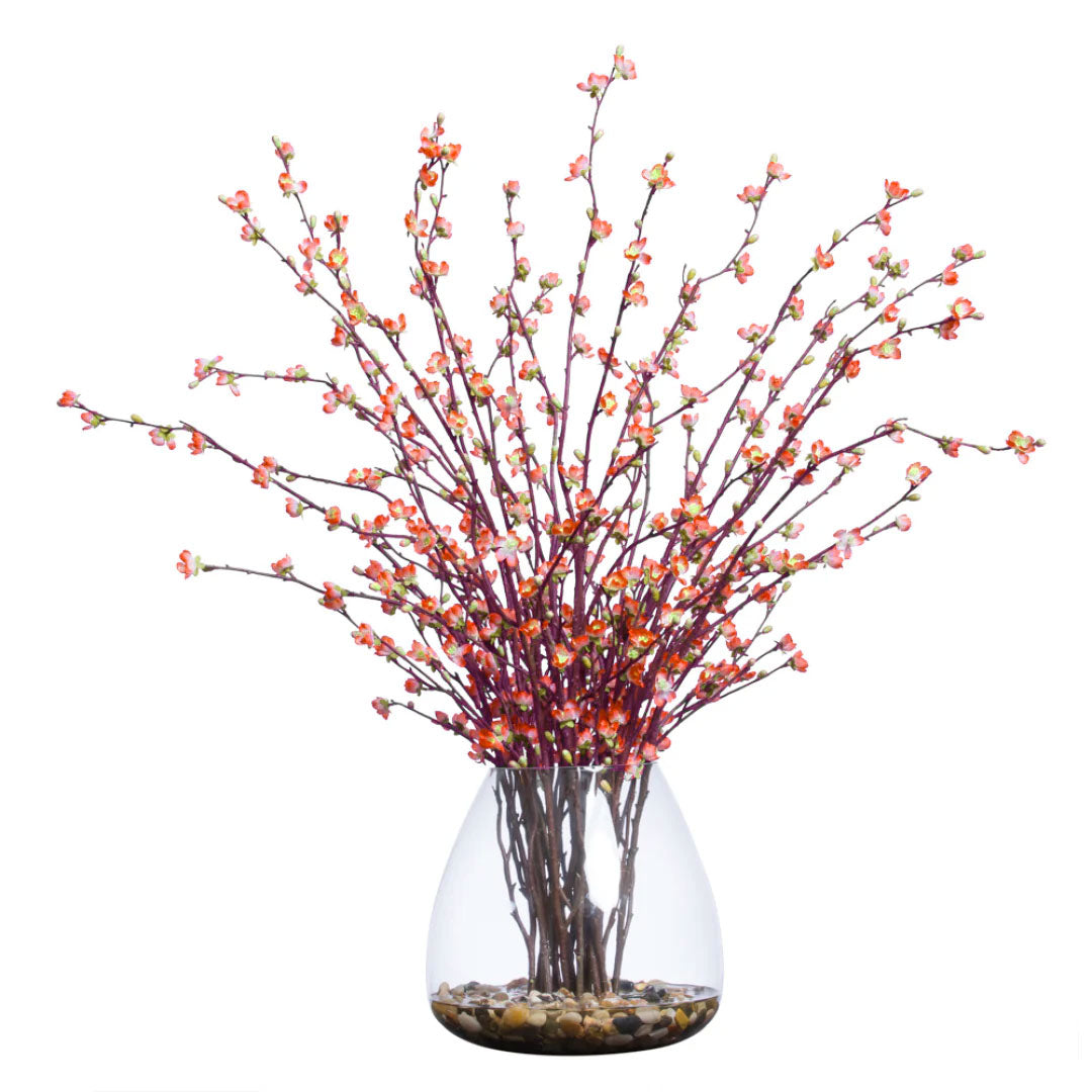 Artificial cherry orange blossom branches in clear vase with decorative stones