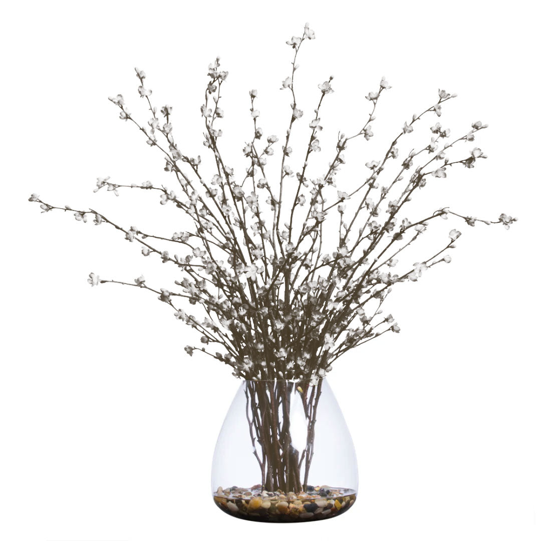 Artificial cherry blossom branches with white flowers in a clear glass vase with pebbles
